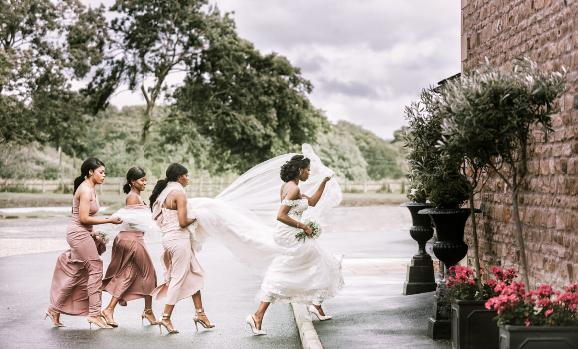 bride outside of the venue with her bridesmaids and maid of honor holding her dress and veil