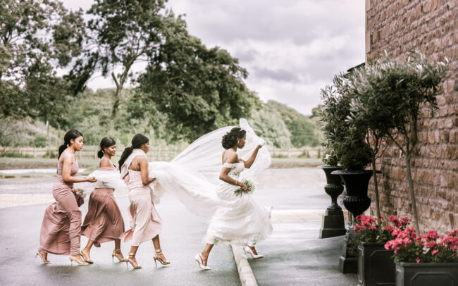 bride outside of the venue with her bridesmaids and maid of honor holding her dress and veil